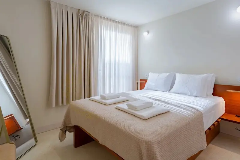Une chambre lumineuse avec un grand lit recouvert d'une courtepointe et de coussins blancs.