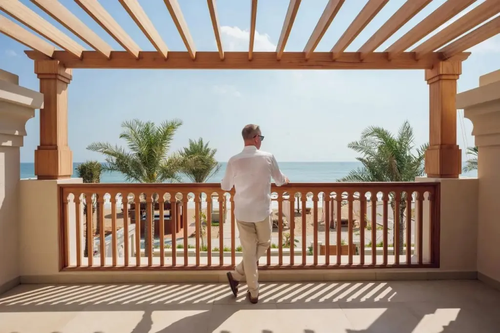 Un homme se tient sur une terrasse en bois avec vue sur la mer et la plage.