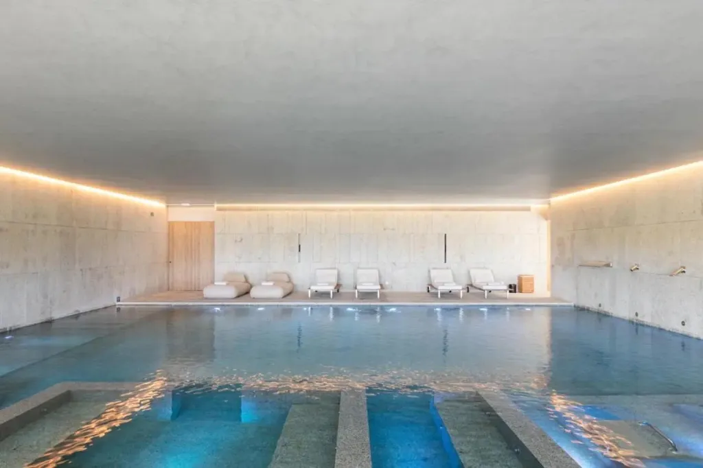 Une piscine intérieure lumineuse avec des transats blancs.