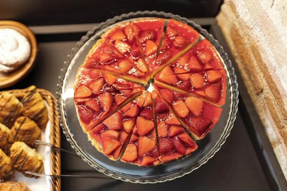 Une tarte aux fraises est présentée sur un présentoir en verre.