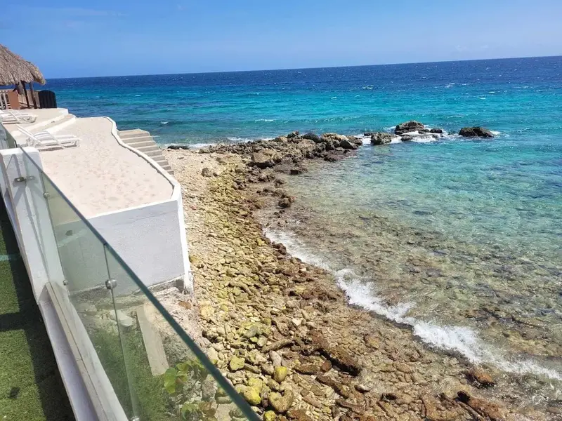 Terrasse ensoleillée surplombant une côte rocheuse et une mer turquoise.