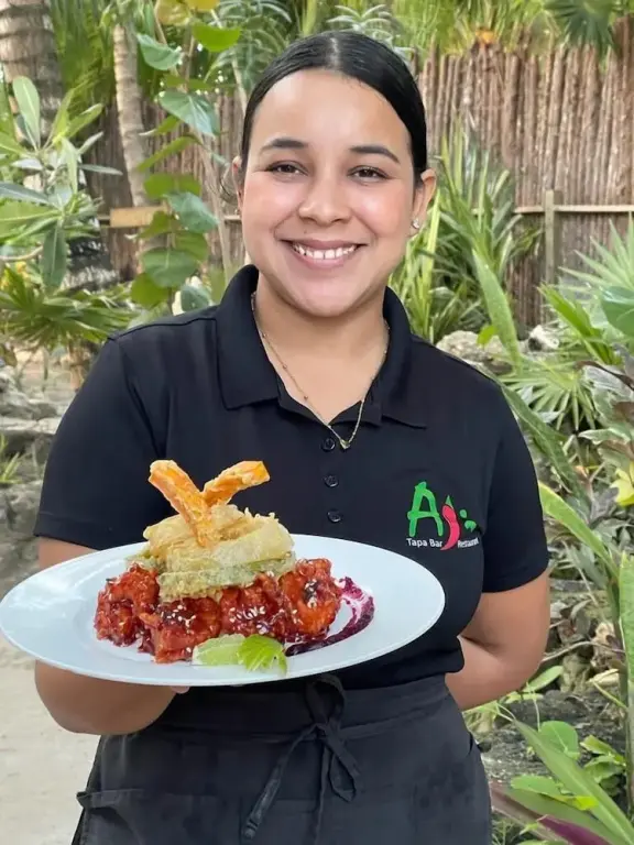 Une personne souriante présente un plat décoré sur une assiette blanche.