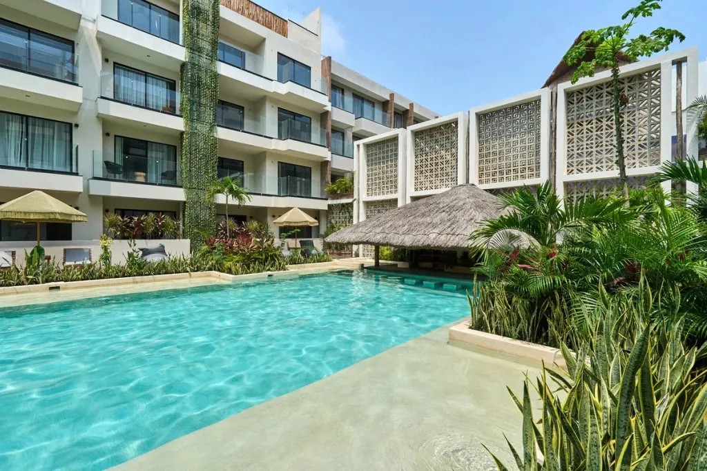 Une piscine turquoise bordée d'une terrasse ensoleillée devant un bâtiment moderne.