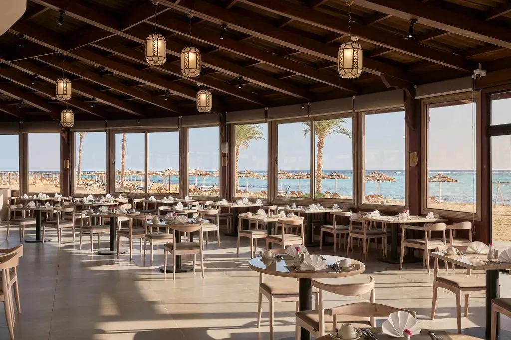 Une salle lumineuse donne sur une plage de sable fin avec des transats.