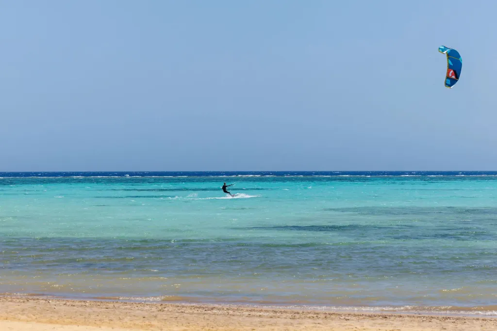 Une personne pratique le kitesurf sur une eau turquoise et peu profonde.