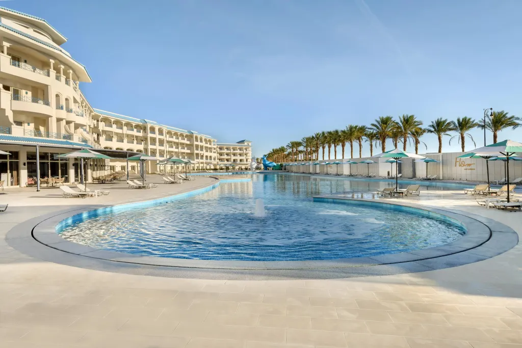 Une grande piscine au bord d'un bâtiment avec des transats et des palmiers.