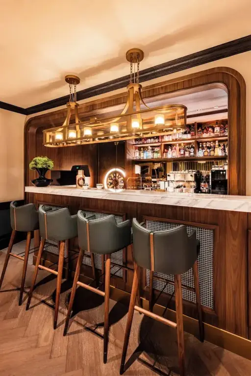 Un comptoir de bar en bois avec des tabourets est éclairé par des suspensions dorées.