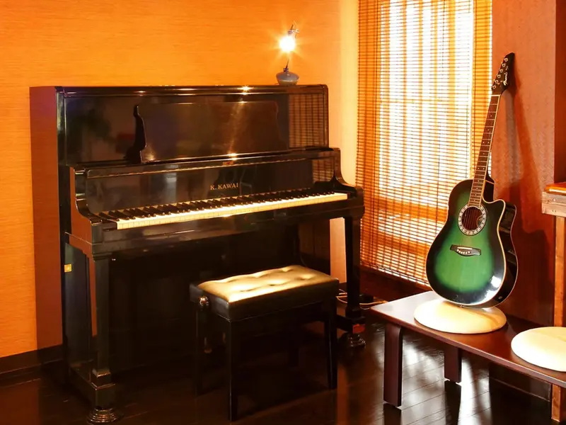 Un piano à queue noir et une guitare reposent dans une pièce aux murs orange et à la fenêtre voilée.
