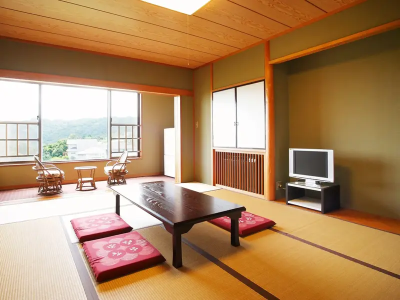 Une pièce lumineuse avec une table basse et des coussins sur un sol en tatami, donnant sur un paysage verdoyant.