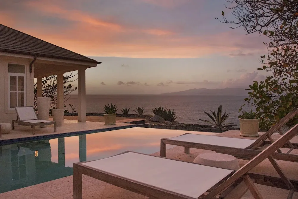 Transats blancs au bord d'une piscine avec vue sur la mer au coucher du soleil.