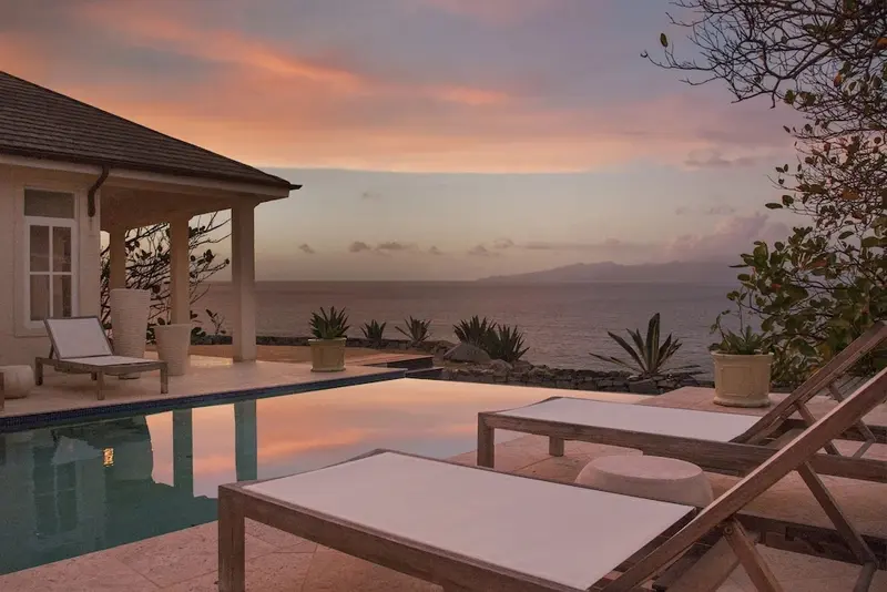 Transats blancs au bord d'une piscine avec vue sur la mer au coucher du soleil.