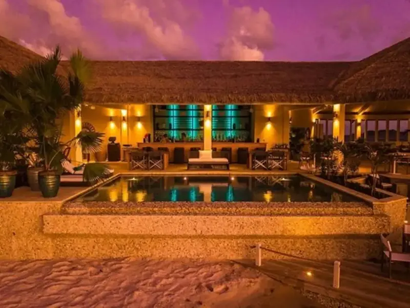 Une piscine illuminée devant un bar en soirée.
