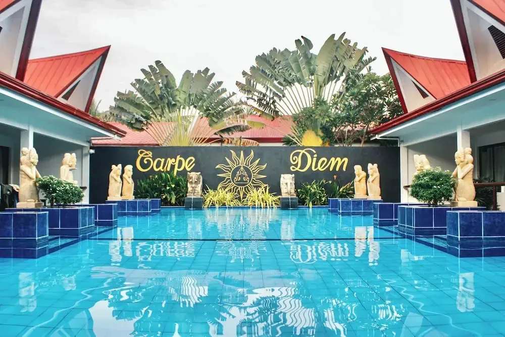 Une piscine rectangulaire turquoise est bordée de statues et de végétation tropicale.