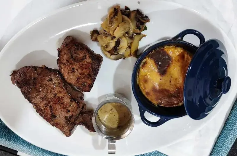 Assiette de viande grillée accompagnée de champignons et d'un gratin.