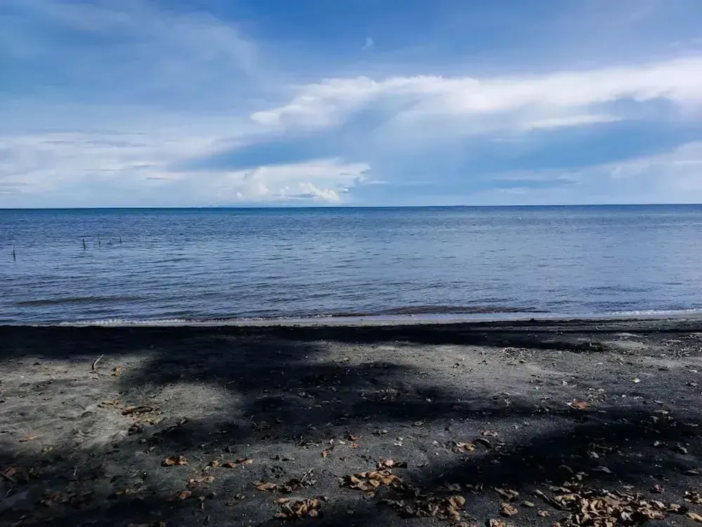 Plage de sable sombre sous un ciel nuageux.