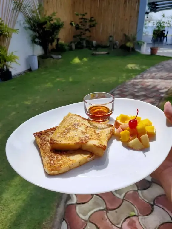 Assiette de pain doré aux fruits frais et sirop sur une terrasse pavée.