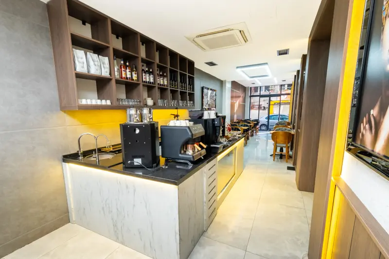 Un comptoir de bar moderne avec des étagères remplies de produits et une salle à manger lumineuse en arrière-plan.