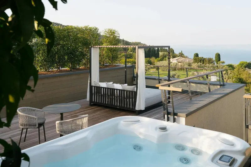 Terrasse aménagée avec jacuzzi et lit à baldaquin offrant une vue sur la végétation et la mer.