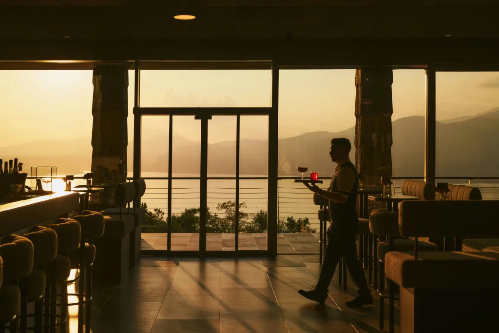 Un serveur porte des boissons à des clients dans un bar avec vue sur la mer.