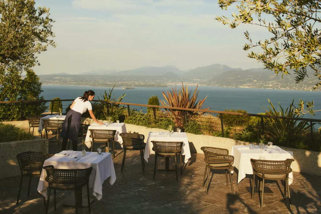 Une terrasse avec des tables dressées offre une vue sur la mer et les montagnes.