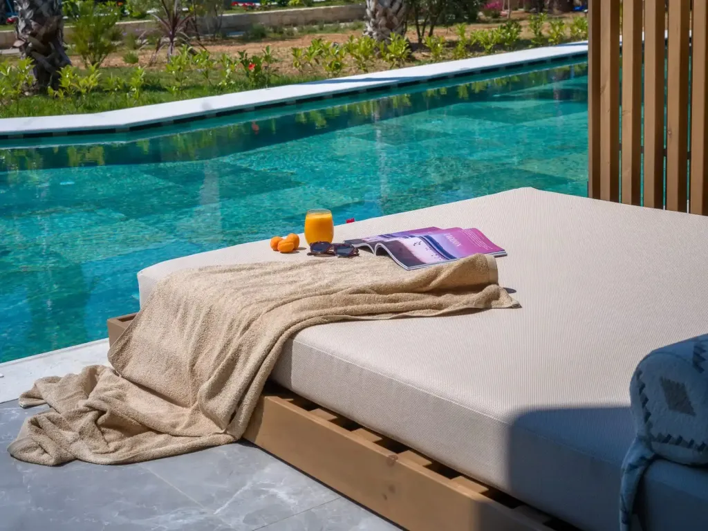 Transat beige avec serviette et boisson au bord d'une piscine turquoise.