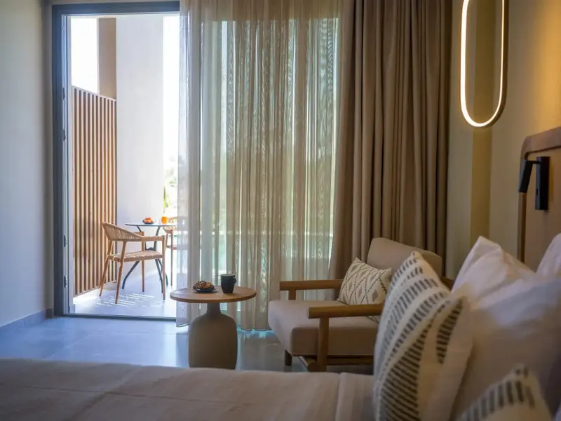 Une chambre lumineuse s'ouvre sur une terrasse avec table et chaises.