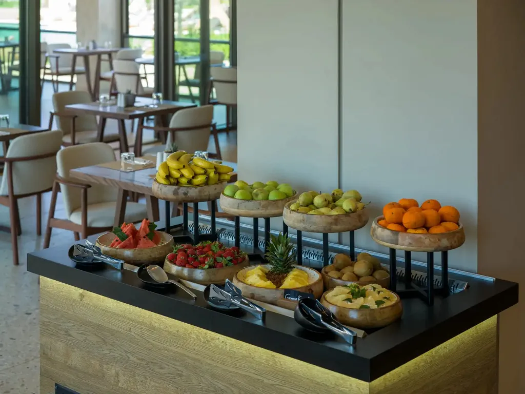 Un buffet de fruits frais est présenté sur un comptoir en bois clair dans une salle lumineuse.