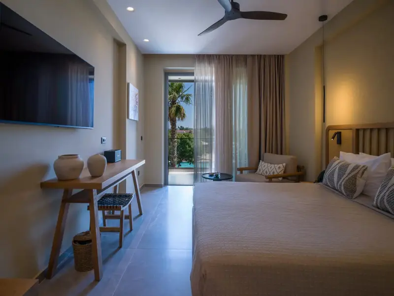 Une chambre lumineuse avec un lit et un espace bureau donnant sur une terrasse.