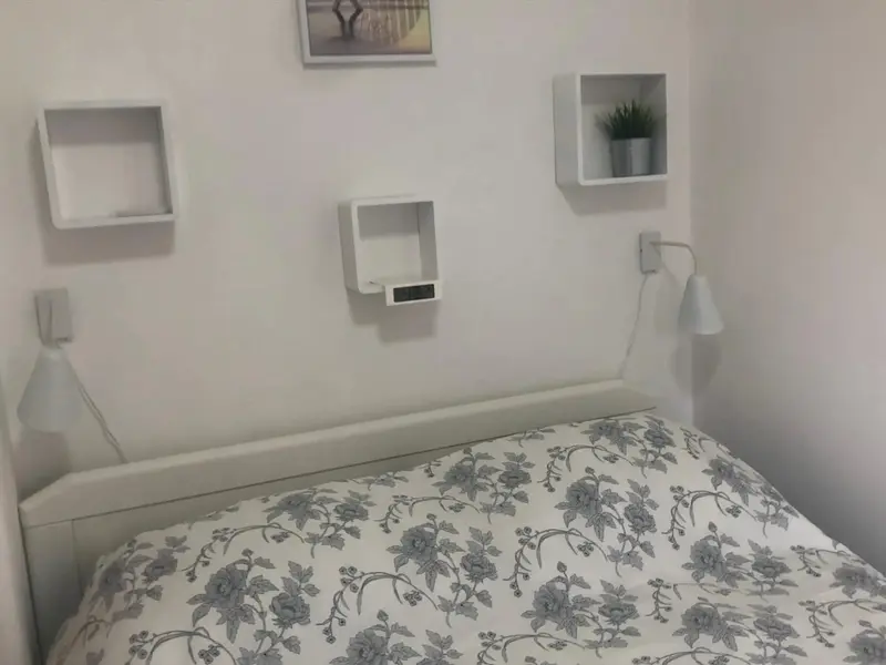 Une chambre lumineuse avec un lit recouvert d'un motif floral et des étagères murales.