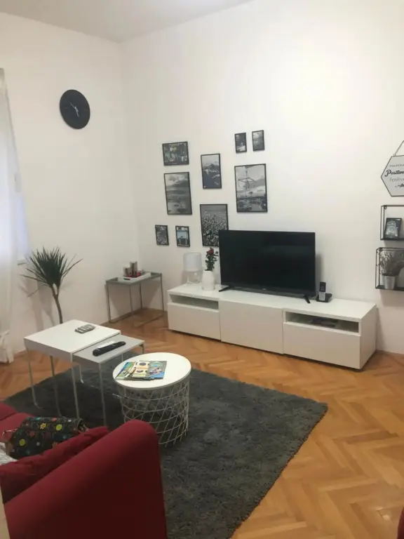 Un salon lumineux avec un canapé rouge et un meuble télé blanc.