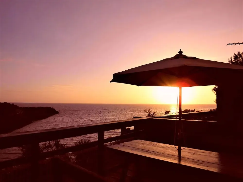 Coucher de soleil sur la mer depuis une terrasse avec un parasol.