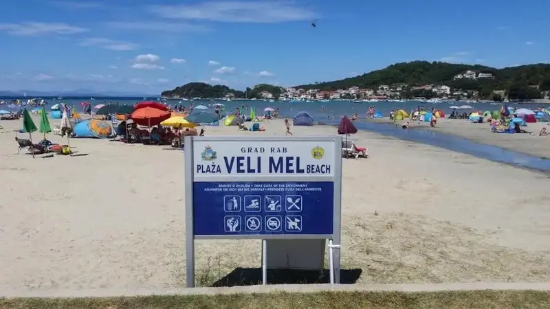Une plage de sable avec des parasols colorés et des personnes se baignant dans une mer calme.