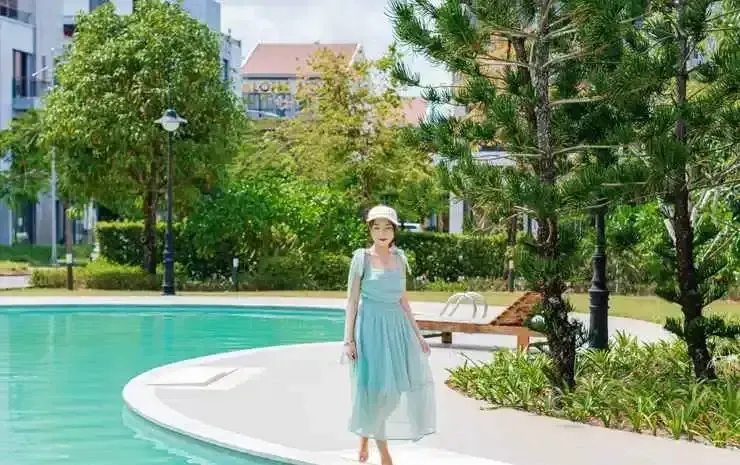 Une femme se tient près d'une piscine ensoleillée, entourée de verdure.