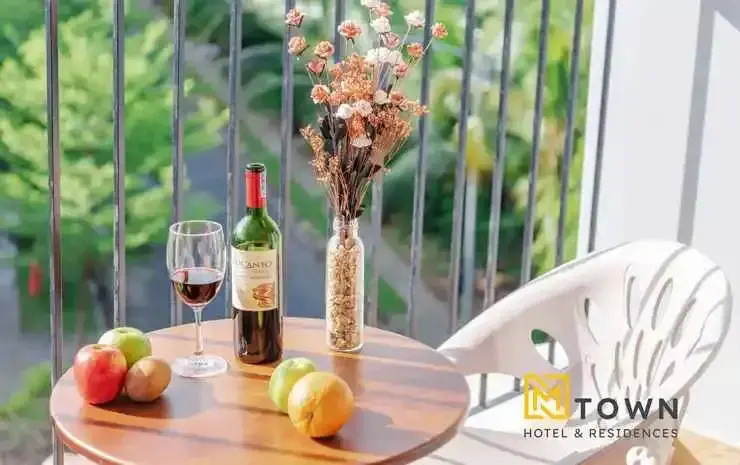 Une table ronde en bois avec une bouteille de vin, des fruits et un vase de fleurs sur une terrasse.