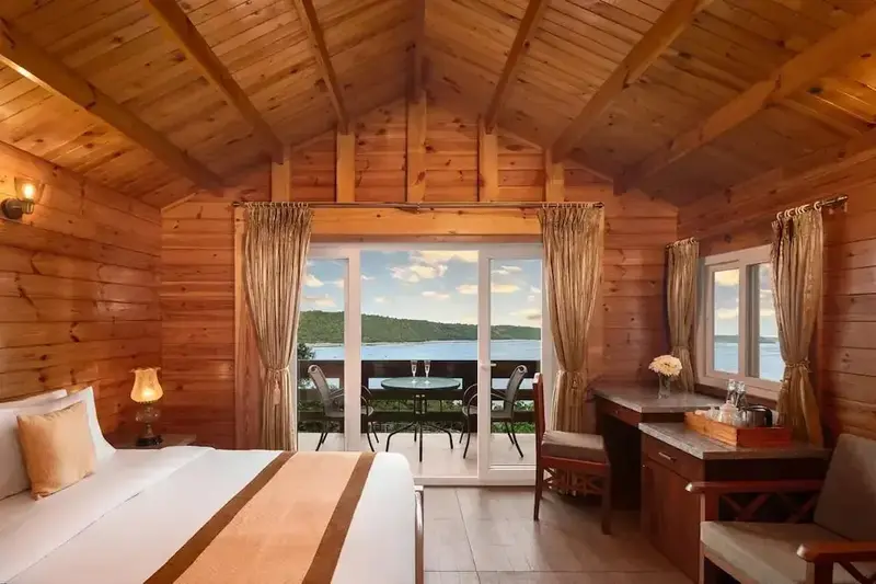 Une chambre lumineuse en bois avec un lit et un accès à une terrasse vue sur mer.