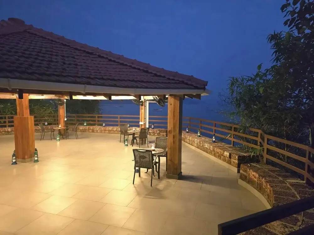 Terrasse lumineuse avec tables et chaises donnant sur la mer au crépuscule.