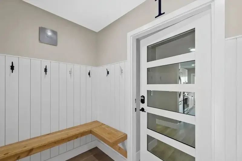 Interieur clair avec un banc en bois et des patères murales.
