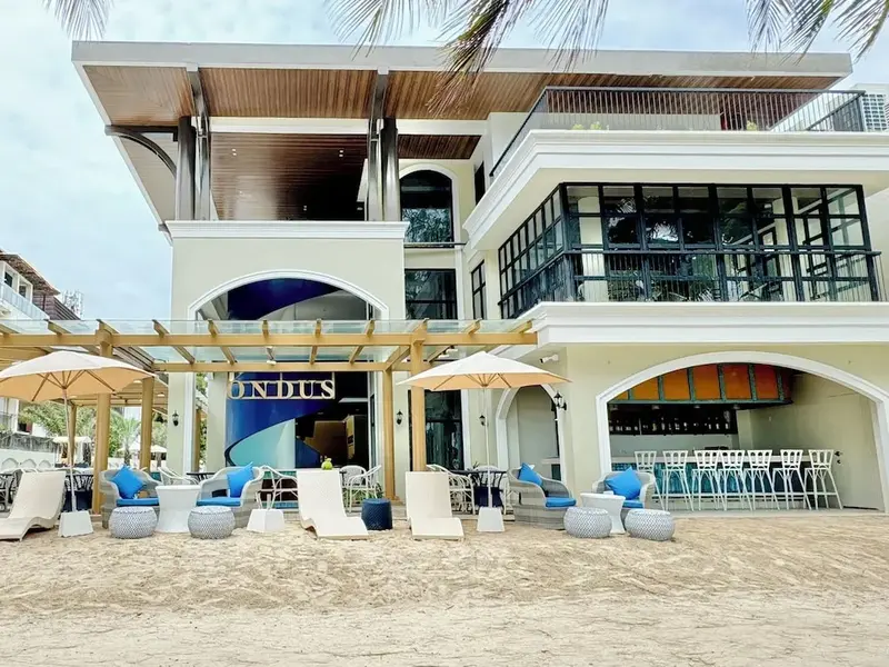 Terrasse de plage avec mobilier d'extérieur et bâtiment moderne en arrière-plan.
