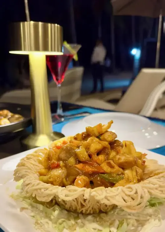 Assiette de pâtes servie à table avec une boisson colorée et une lampe décorative.