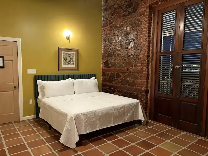 Une chambre lumineuse avec un lit recouvert d'une courtepointe blanche et un mur en pierre.