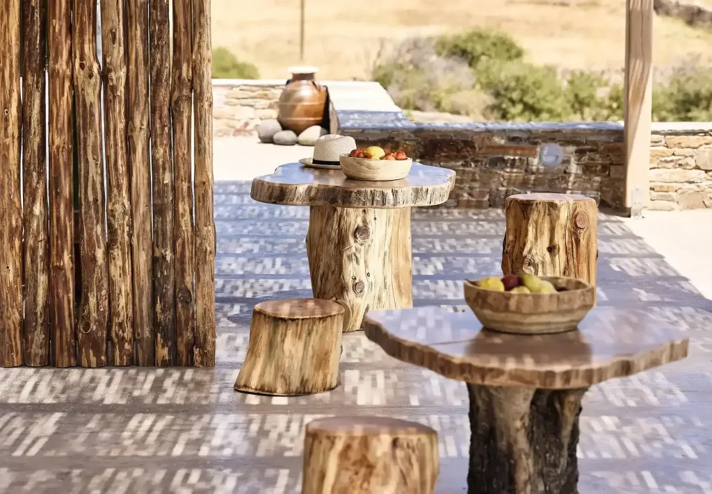 Petites tables et tabourets en bois brut sur une terrasse ensoleillée.