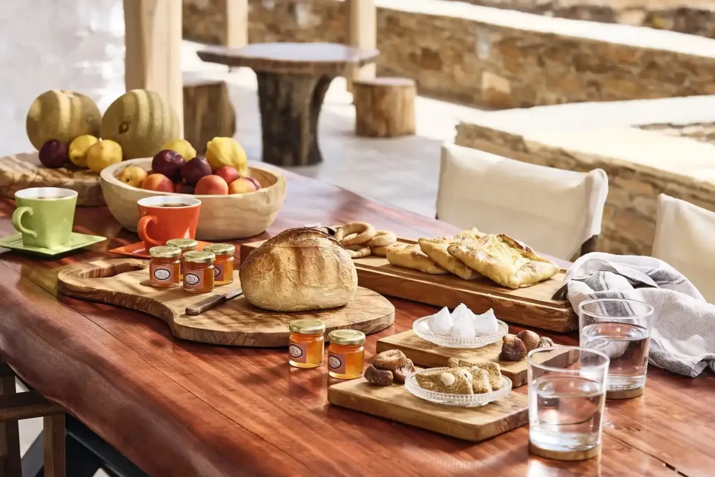 Une table en bois est dressée avec des fruits frais, du pain, des confitures et des pâtisseries.