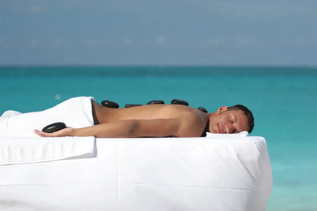Un homme reçoit un massage aux pierres chaudes en bord de mer.