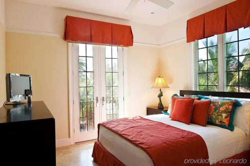 Une chambre lumineuse avec un lit recouvert d'une courtepointe rouge et des oreillers colorés, donnant sur un jardin tropical.