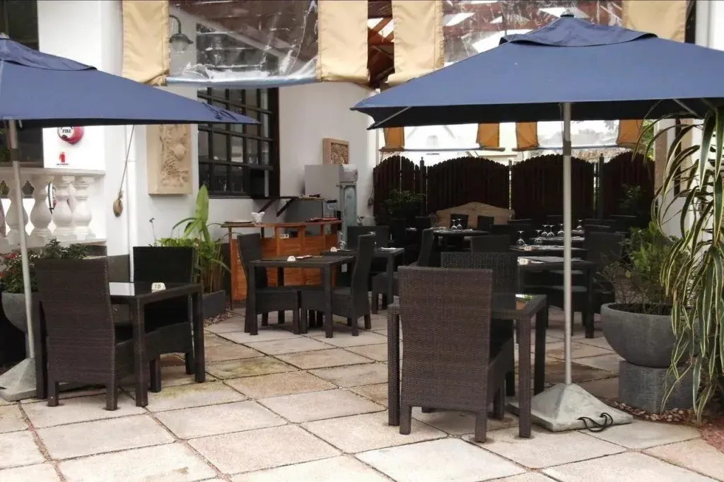 Terrasse ombragée avec tables et chaises pour les repas.
