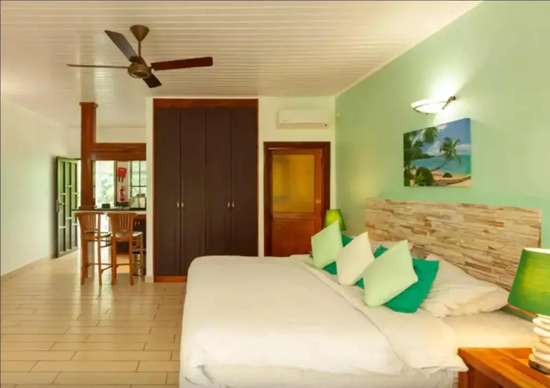 Une chambre lumineuse avec un grand lit et un espace cuisine en fond.