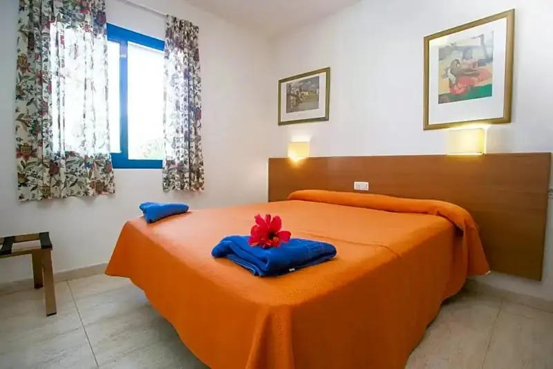 Une chambre lumineuse avec un grand lit recouvert d'une couverture orange et de fleurs.