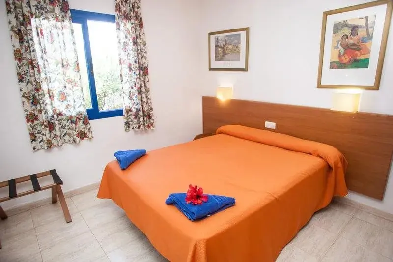 Une chambre lumineuse avec un lit recouvert d'une couverture orange et des rideaux fleuris.