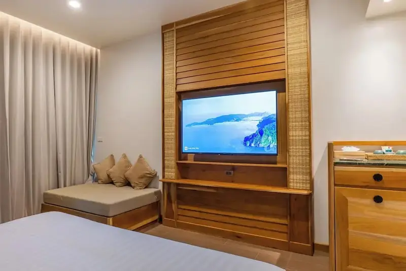 Une télévision est fixée au-dessus d'un meuble en bois dans une chambre lumineuse.