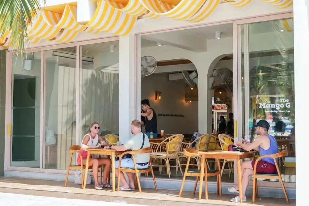 Des clients sont assis à des tables en bois devant un restaurant ensoleillé.